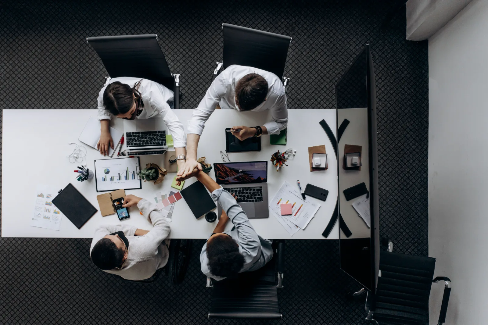Equipo de trabajo reunido alrededor de una mesa con laptops y documentos, visto desde arriba